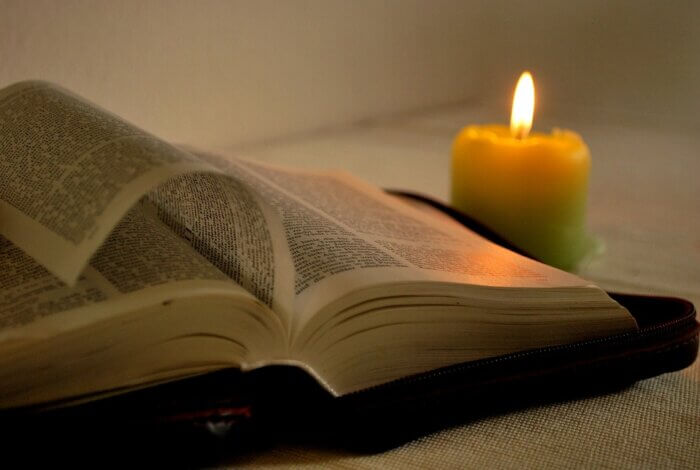 a candle burns warmly by an open bible